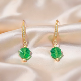 A pair of gold drop earrings with small pavé-set clear stones and green faceted clover crystals drops, displayed on a white marble surface.