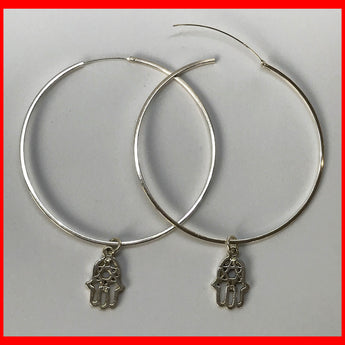 A pair of large silver hoop earrings with a Hamsa charm dangle.