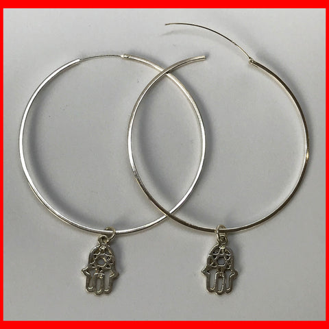 A pair of large silver hoop earrings with a Hamsa charm dangle.