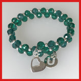 A green crystal bracelet with sterling silver charms and beads, featuring a heart and a 'U' charm, on a memory wire band.