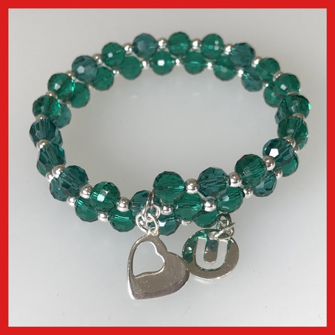 A green crystal bracelet with sterling silver charms and beads, featuring a heart and a 'U' charm, on a memory wire band.