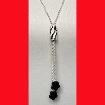 A long necklace featuring a zebra column design with sterling silver and two black onyx charms at the bottom, displayed against a red background.